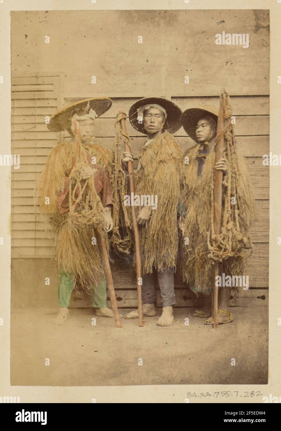 Three Japanese men in grass robes and wide-brimmed hats. Stock Photo