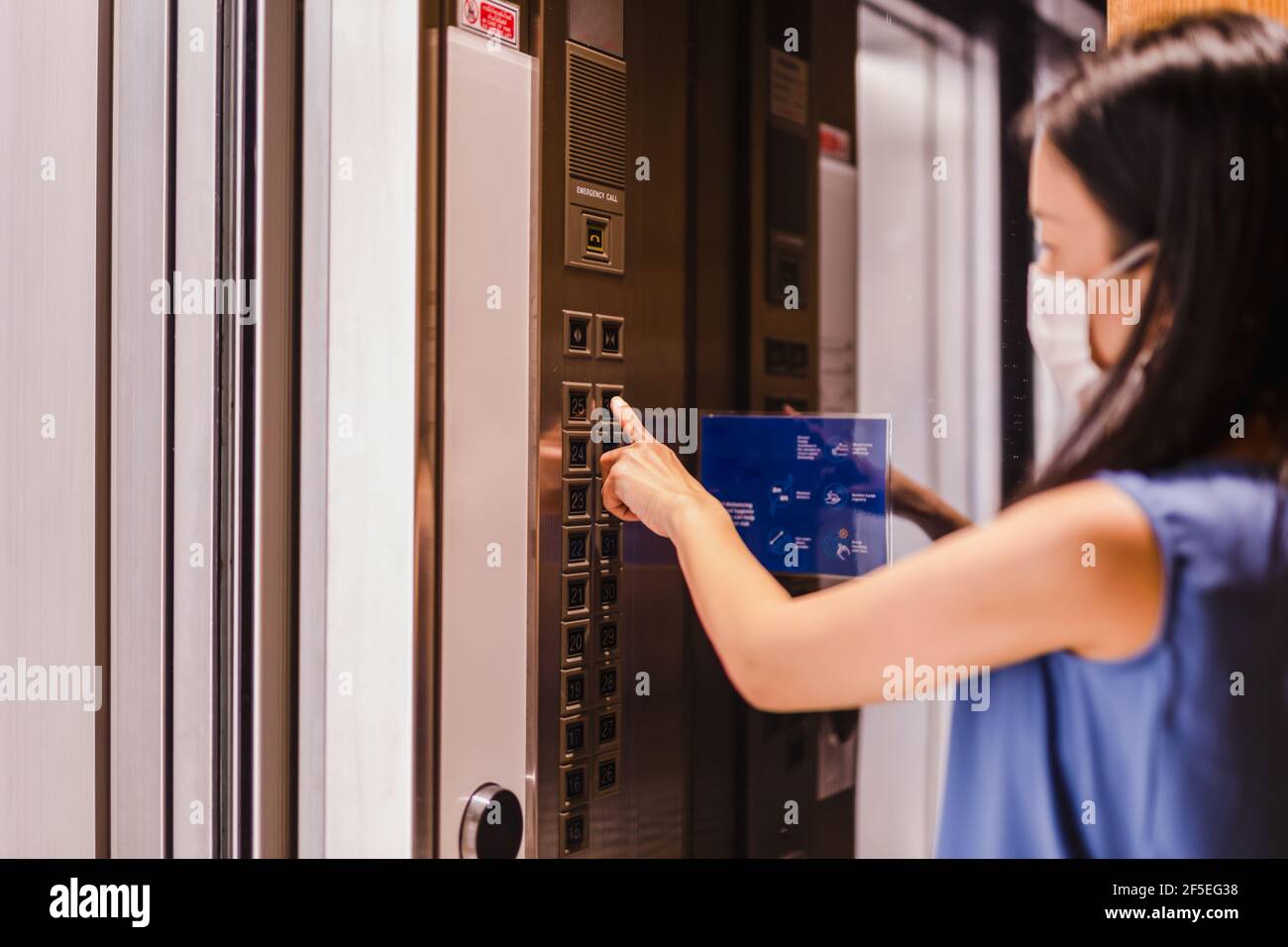 Woman in face mask pressing elevator button. Stock Photo
