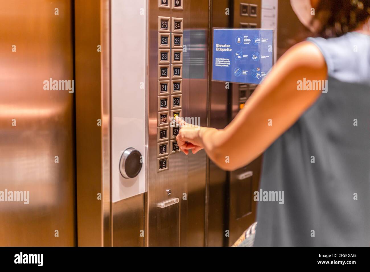 Woman in face mask pressing elevator button. Stock Photo