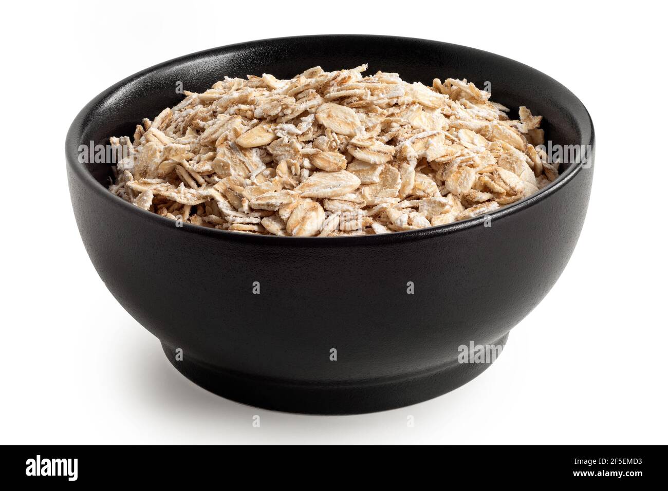 Uncooked porridge oats in a black ceramic bowl isolated on white Stock