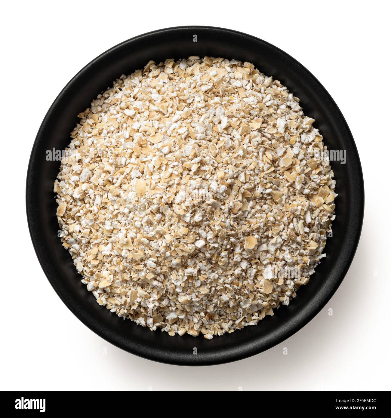 Uncooked coarse oatmeal in a black ceramic bowl isolated on white. Top view. Stock Photo