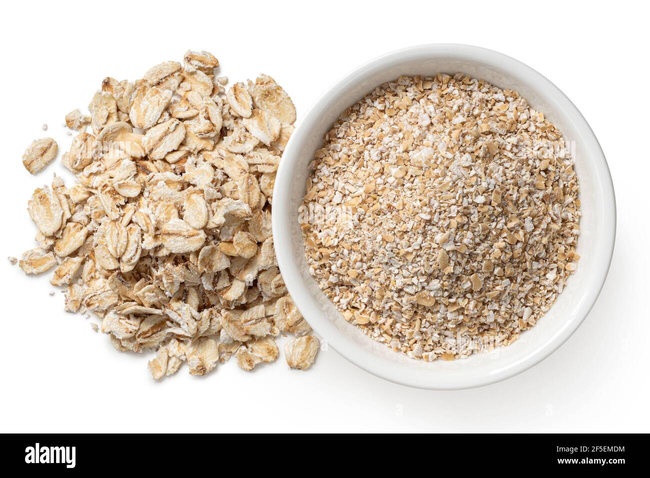 Uncooked coarse oatmeal in a white ceramic bowl next to a pile of uncooked porridge oats isolated on white. Top view. Stock Photo