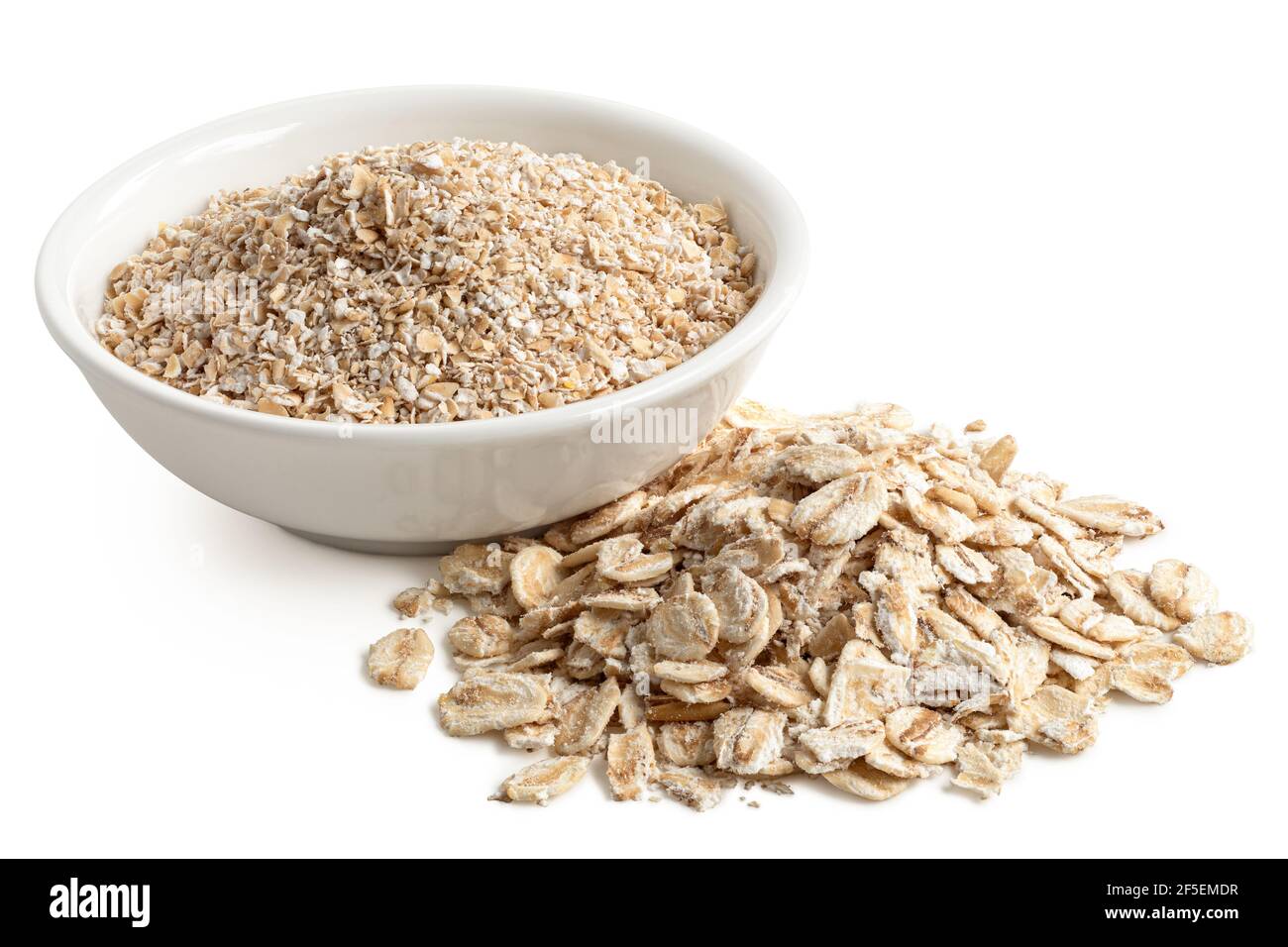 Uncooked coarse oatmeal in a white ceramic bowl next to a pile of uncooked porridge oats isolated on white. Stock Photo