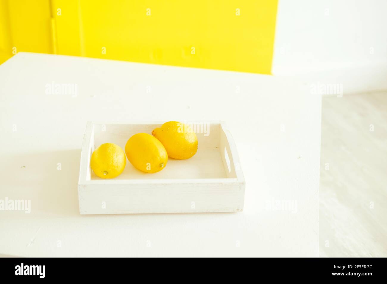 bright yellow lemons on a yellow background. Lemons on a white tray. Contrast photography with the color of the year. Stylish decor. Citrus fruits Stock Photo