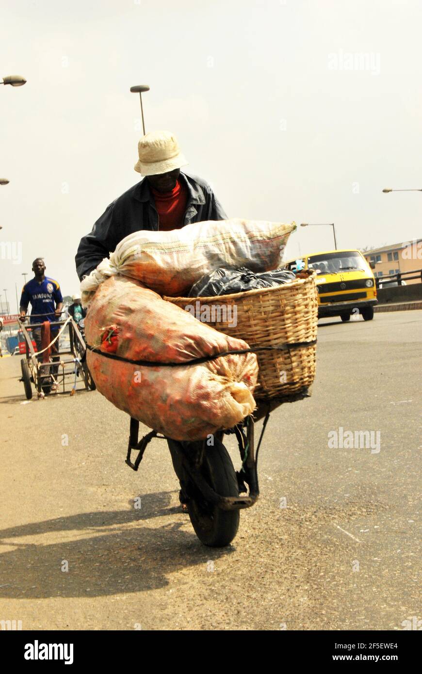 8. Lagos Metro: A man pushing a wheelbarrow loaded with tomatoes at Oshodi Market, Lagos, Nigeria for daily survival. Stock Photo