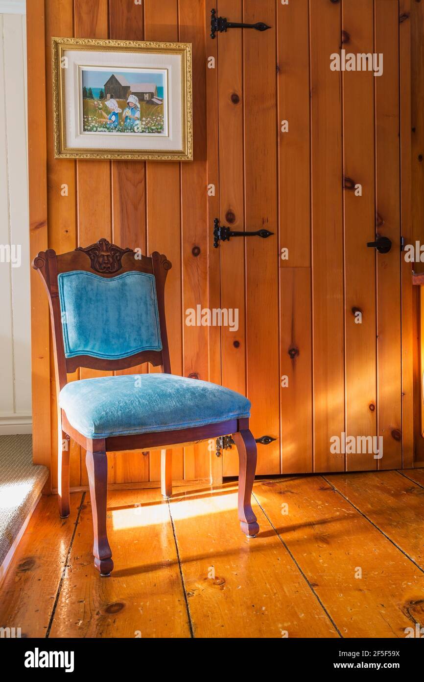 Antique walnut wood chair with upholstered blue velvet seat and backrest carved with gargoyle's head in hallway with wide plank pine wood floorboards Stock Photo