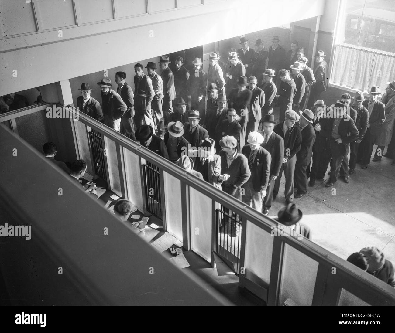 Unemployment benefits aid begins. Line of men inside a division office of the State Employment Service office at San Francisco, California, waiting to register for benefits on one of the first days the office was open. They will receive from six to fifteen dollars per week for up to sixteen weeks. Coincidental with the announcement that the federal unemployment census showed close to ten million persons out of work, twenty-two states begin paying unemployment compensation. January 1938. Photograph by Dorothea Lange. Stock Photo