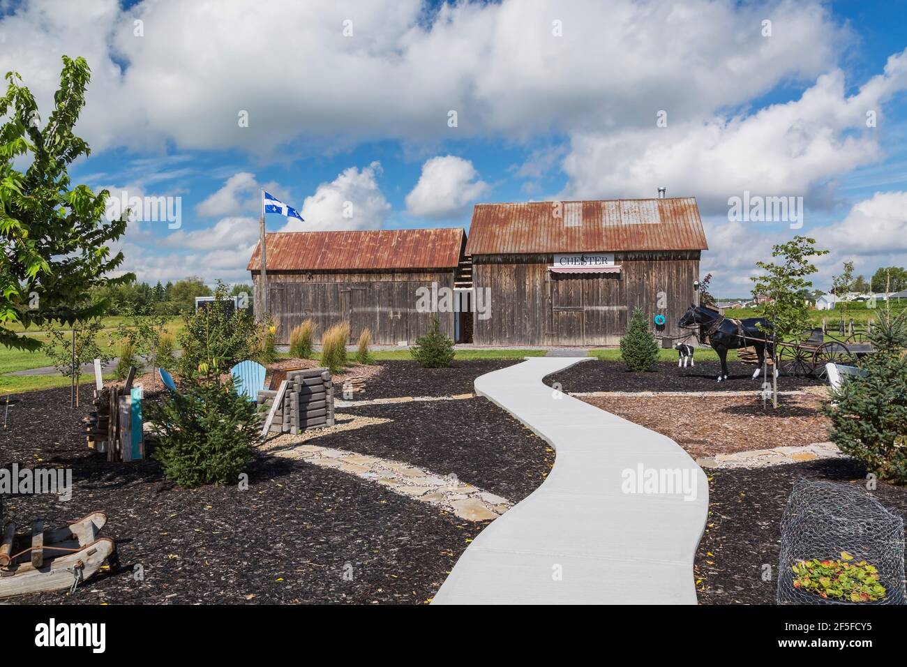 Black mulch borders and cement footpath leading to old wood plank barns