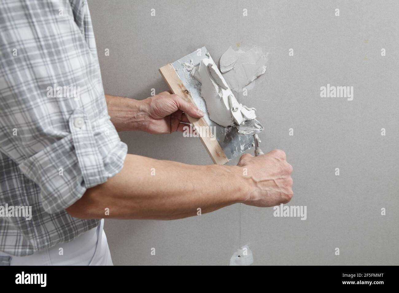 closeup hands man drywall worker or plasterer putting stucco on plasterboard wall using a trowel