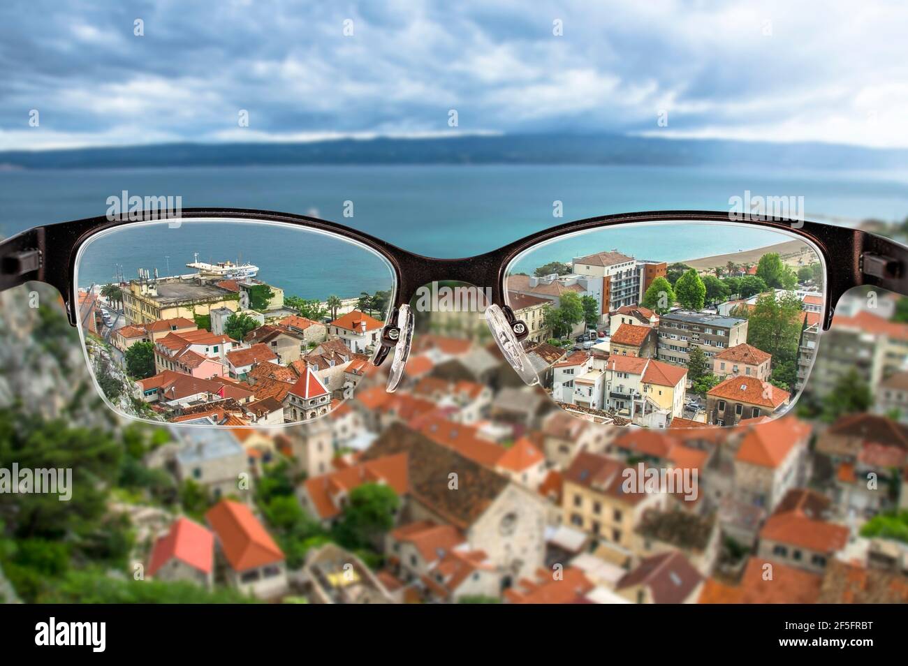 Red roofs and blue sea in Croatian city landscape focused in women's glasses frame. View through eyeglasses. Better vision concept. Stock Photo