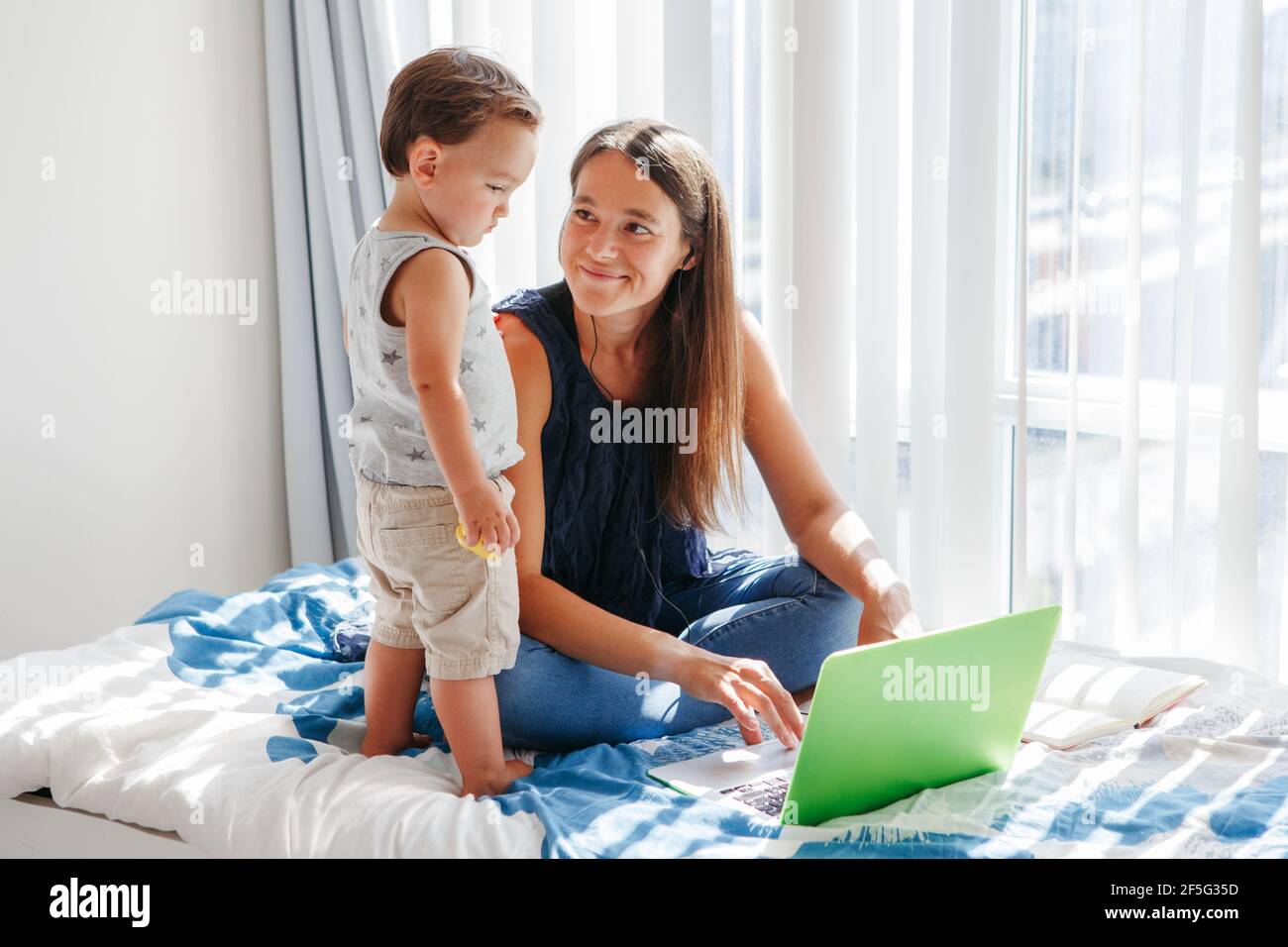 Work from home with kids. Mother working on laptop with baby boy toddler at home. Remote work