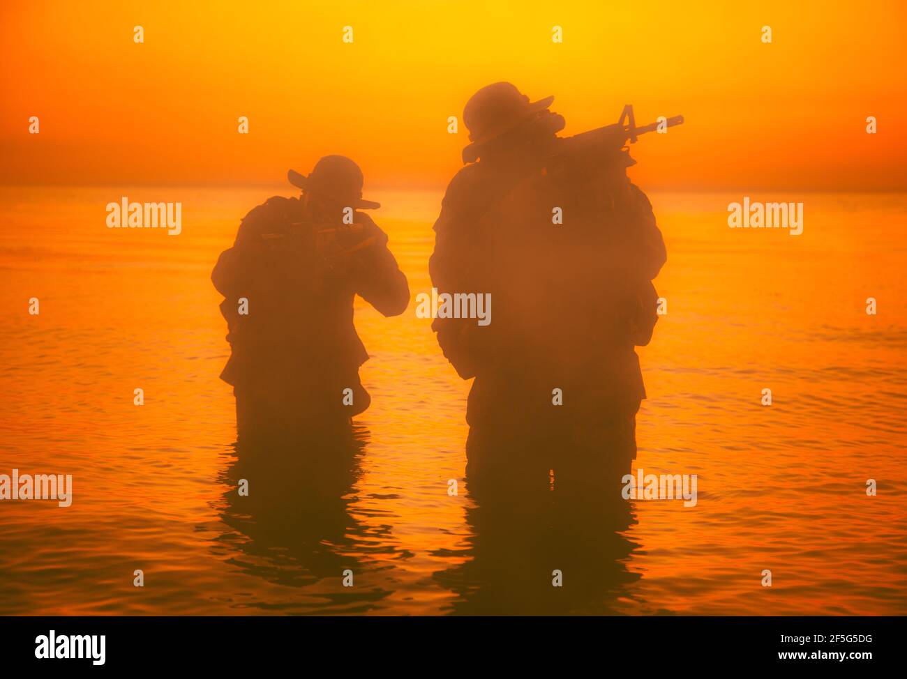 Commando soldiers walking in water, army special operations forces fighters sneaking in darkness, aiming assault rifles and observing shore during amphibious operation on coast at night or dawn Stock Photo
