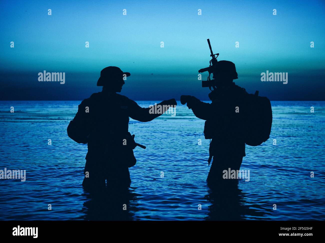 Army special operations forces soldiers, commando fighters doing fist dump gesture while standing knee-deep in water. Two Marines shooters or coast guard fighters celebrating mission successful ending Stock Photo