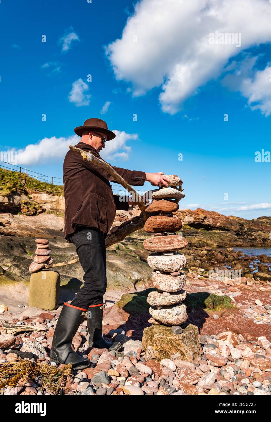 James Craig Page, stone stacker, stacking stones to create a rock sculpture on Eye Cave beach, Dunbar, East Lothian, Scotland, UK Stock Photo