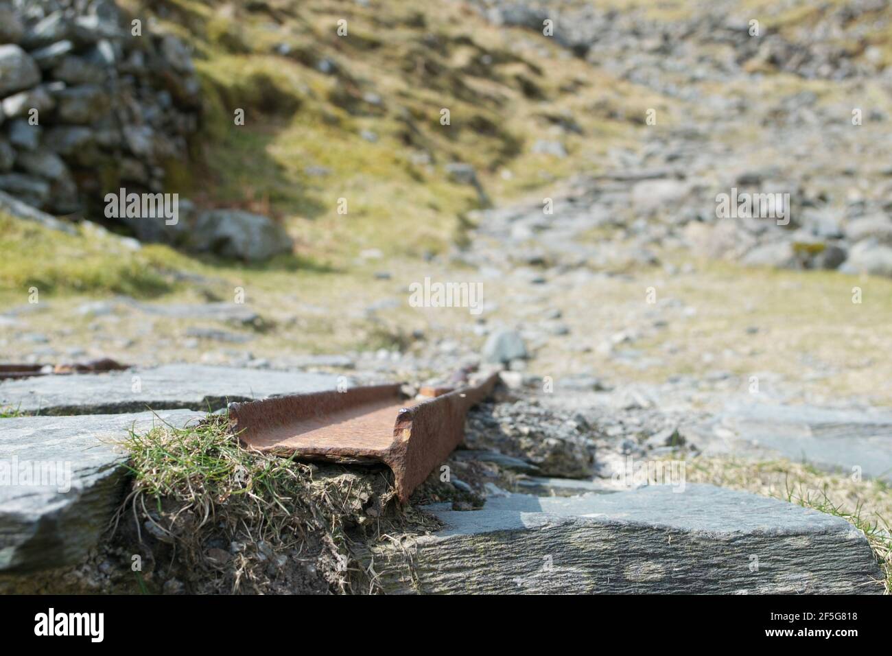 The remains of mining works: rusty metal railway tracks at an old slate quarry in the mountains. Close up on the equipment; a track between the rocks Stock Photo