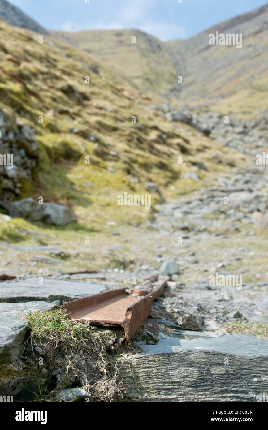 The remains of mining works: rusty metal railway tracks at an old slate quarry in the mountains. Close up on the equipment; a track between the rocks Stock Photo