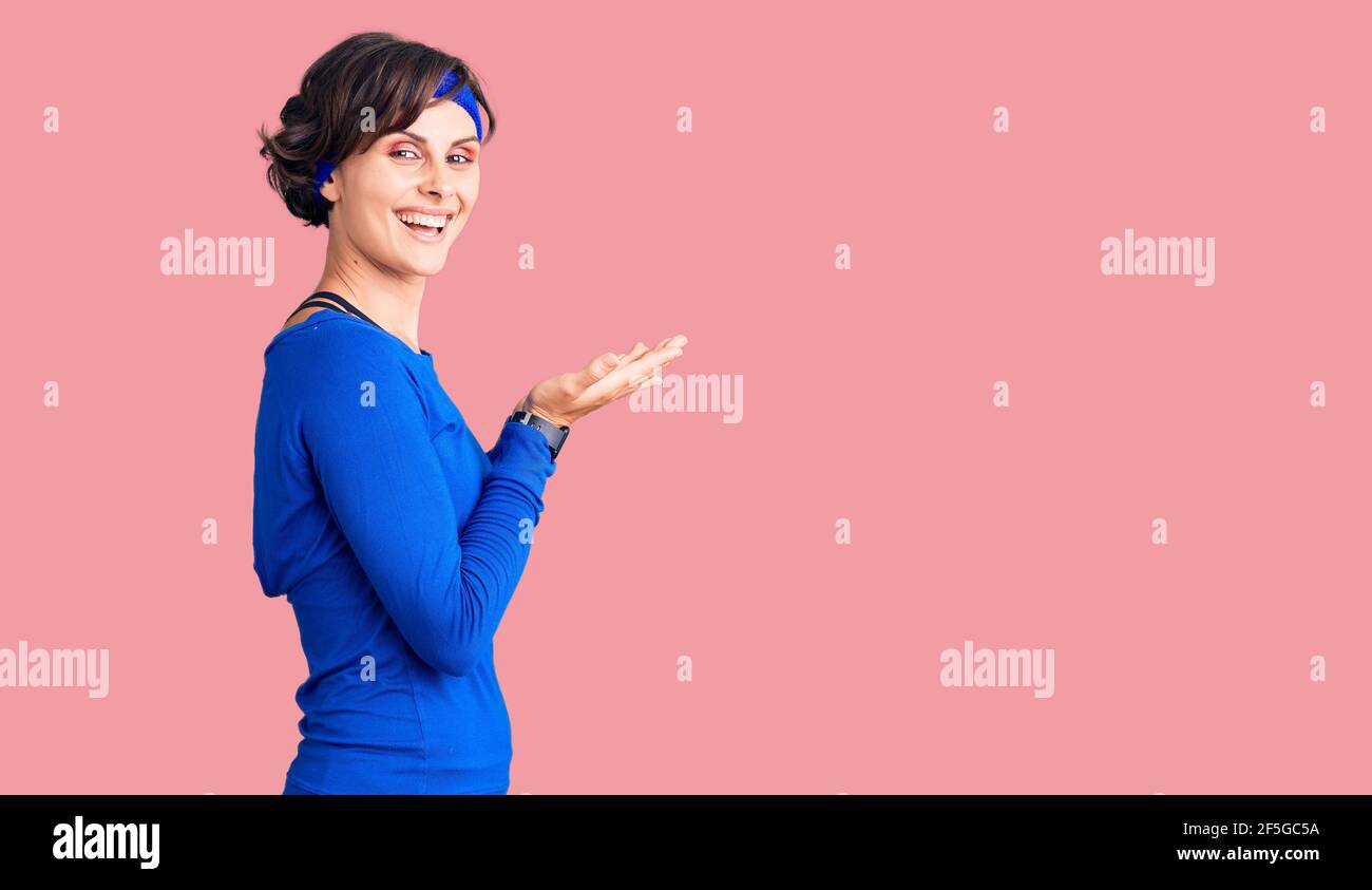 Beautiful young woman with short hair wearing training workout clothes pointing aside with hands open palms showing copy space, presenting advertiseme Stock Photo