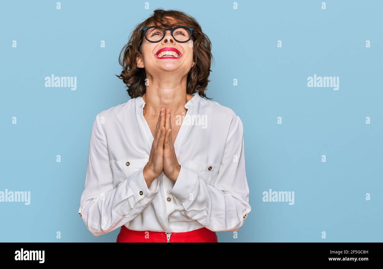 Young hispanic woman wearing business style and glasses begging and praying with hands together with hope expression on face very emotional and worrie Stock Photo