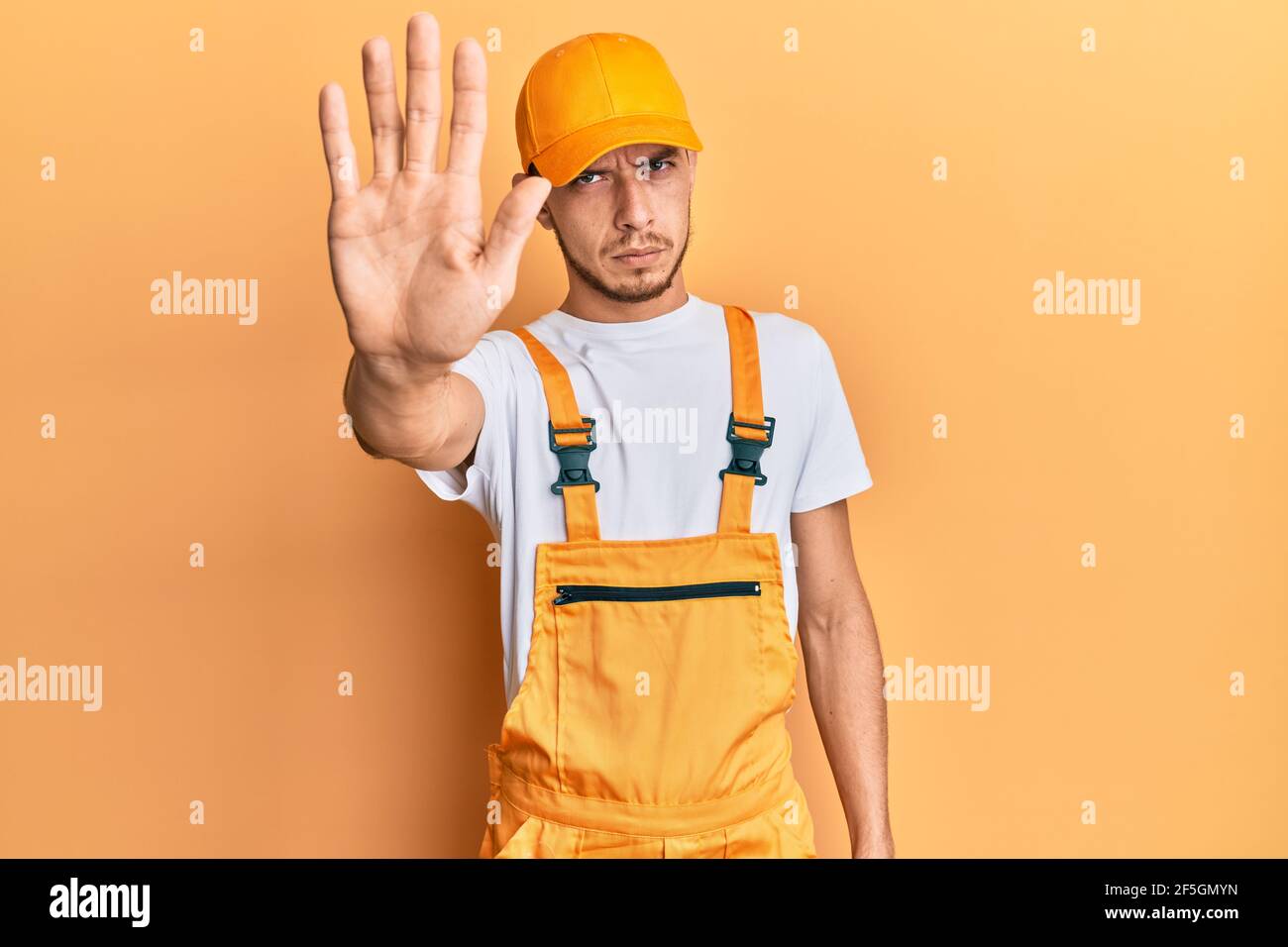 Hispanic young man wearing handyman uniform doing stop sing with palm ...