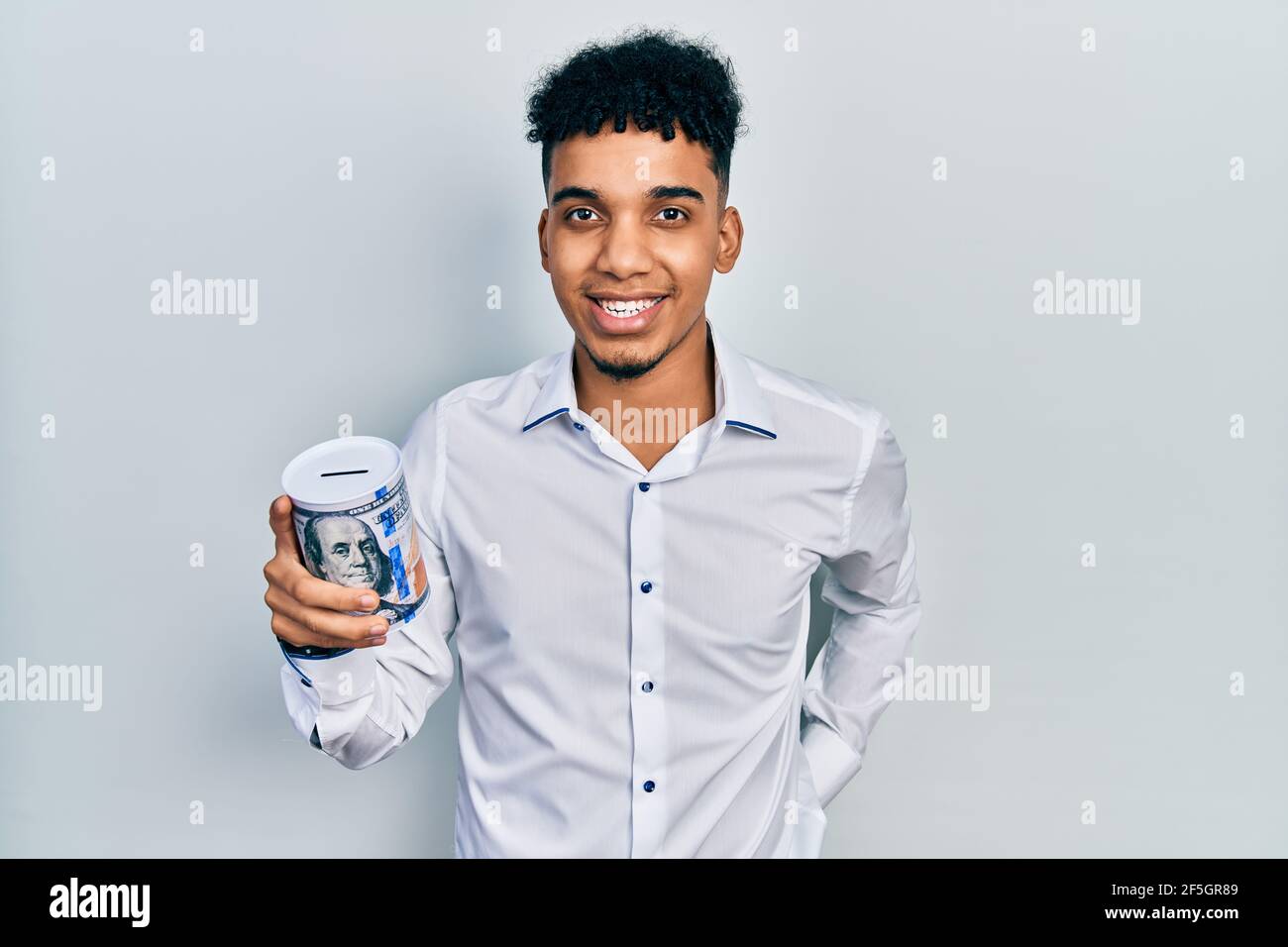 Young african american man holding piggy bank looking positive and ...