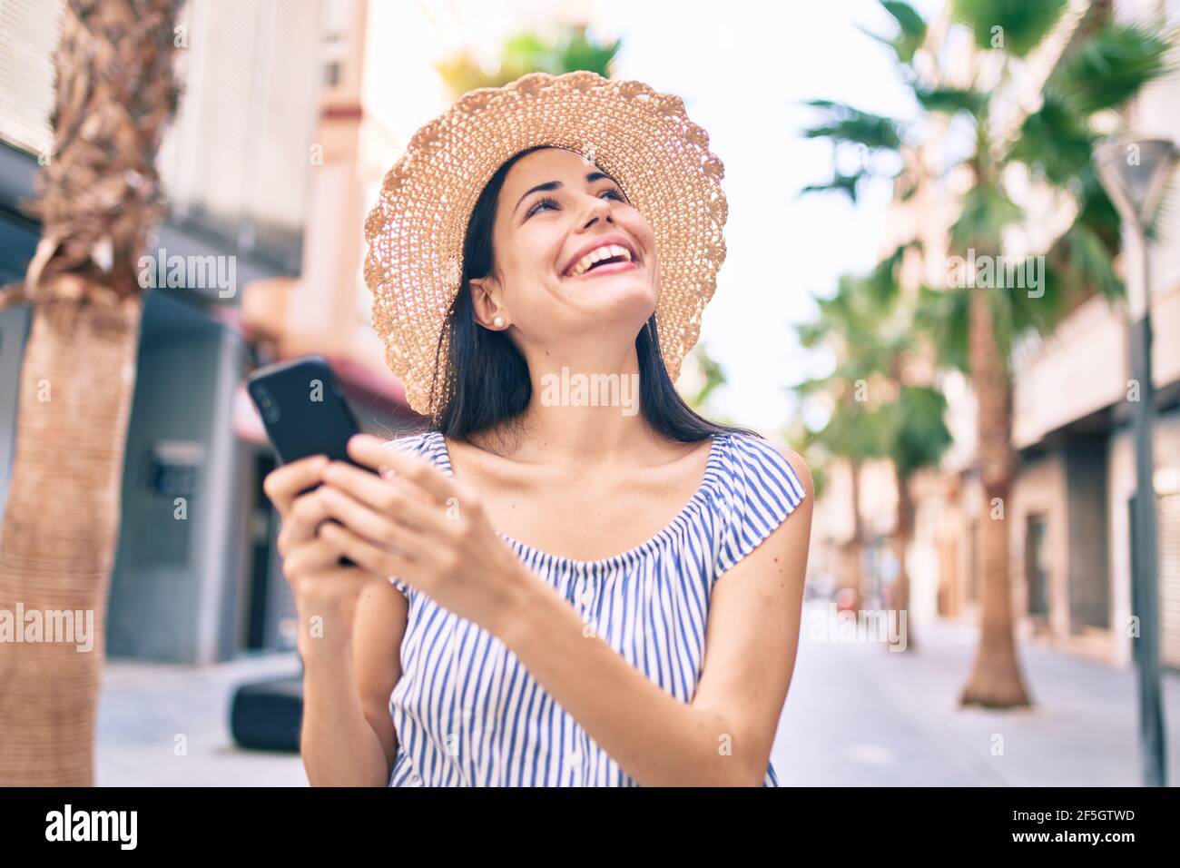 Young latin tourist girl on vacation smiling happy using smartphone at ...
