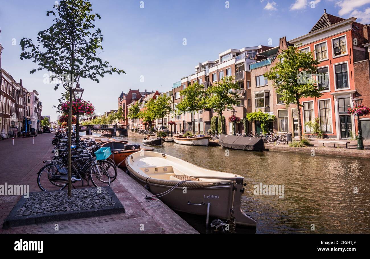 Boats parked along canal in Leiden, The Netherlands. Bunch of bikes standing next to the canal. Sunny summer day Stock Photo