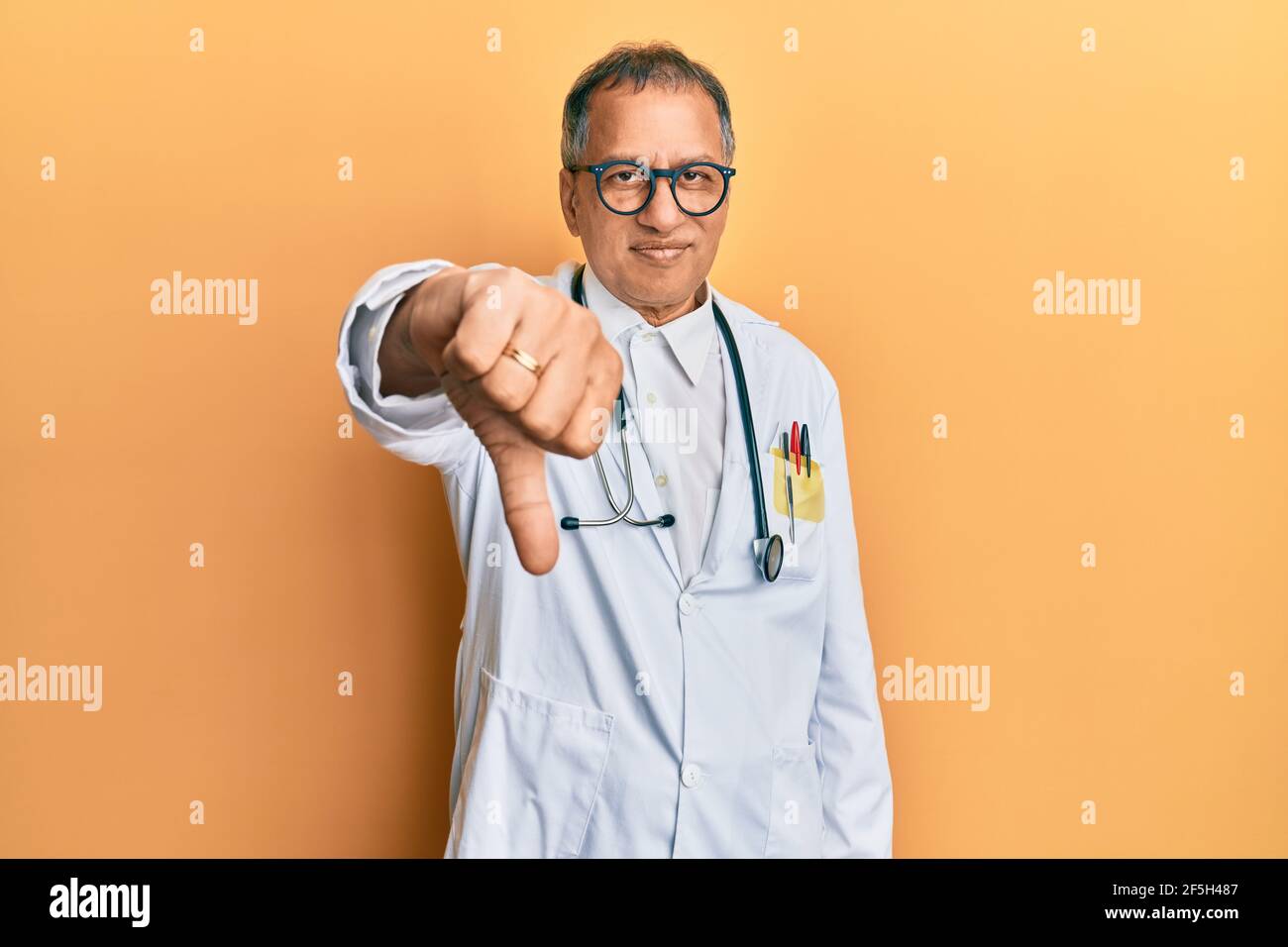 Middle age indian man wearing doctor coat and stethoscope looking ...