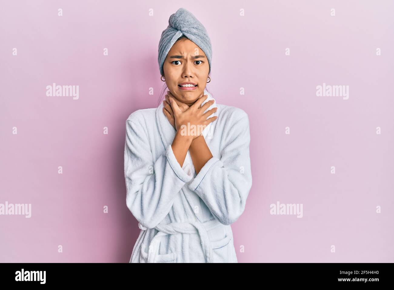 Young chinese woman wearing shower towel cap and bathrobe shouting and suffocate because painful
