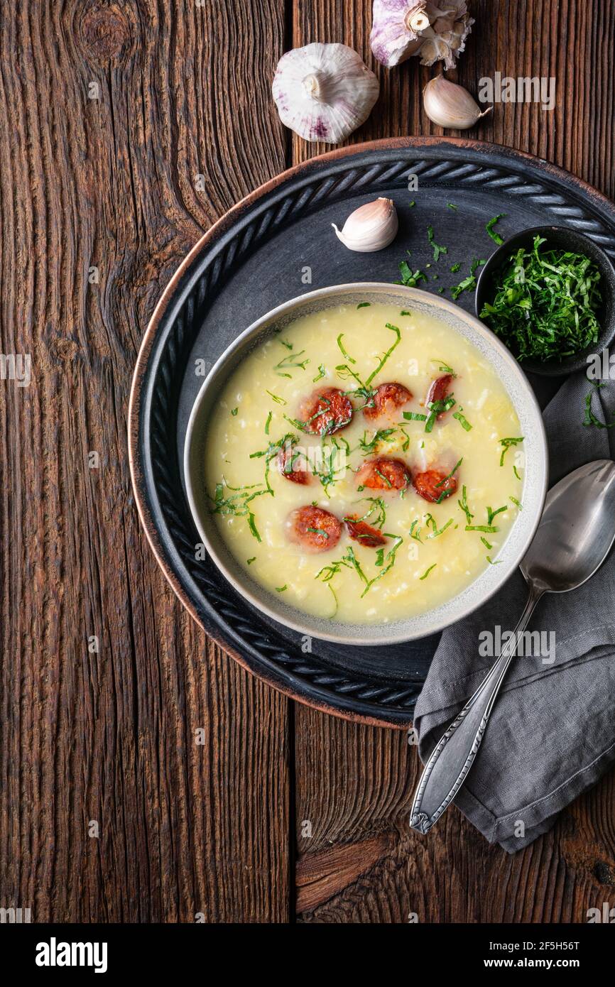 Caldo Verde soup made of savoy cabbage, pureed potatoes, onion, garlic and fried sausage slices in a ceramic bowl  on rustic wooden background Stock Photo