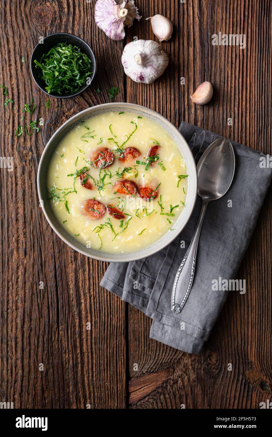 Caldo Verde soup made of savoy cabbage, pureed potatoes, onion, garlic and fried sausage slices in a ceramic bowl  on rustic wooden background Stock Photo