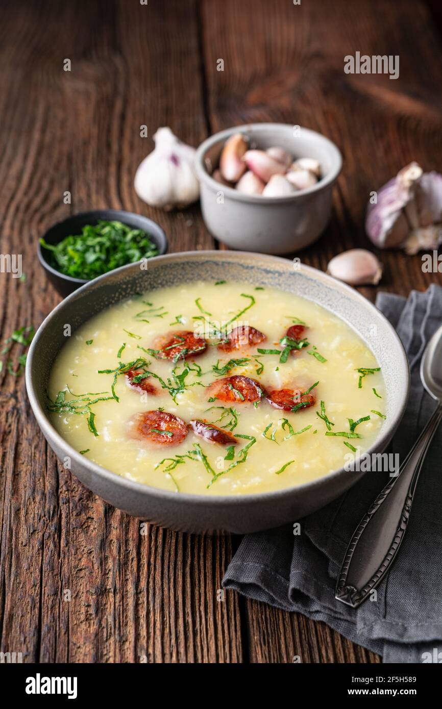 Caldo Verde soup made of savoy cabbage, pureed potatoes, onion, garlic and fried sausage slices in a ceramic bowl  on rustic wooden background Stock Photo