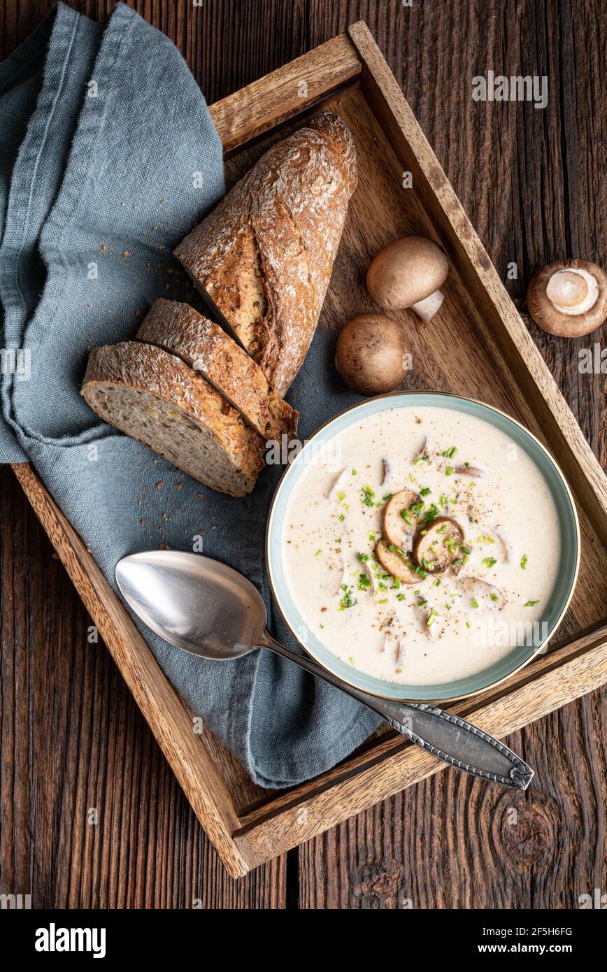 Delicious lunch, comforting Cream of mushroom soup topped with freshly chopped chives, served with crusty bread on rustic wooden background Stock Photo