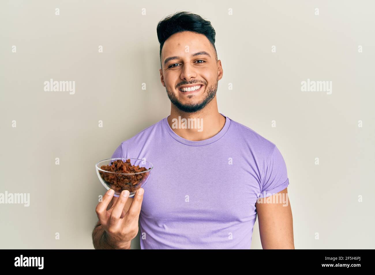 Young arab man holding raisins bowl looking positive and happy standing