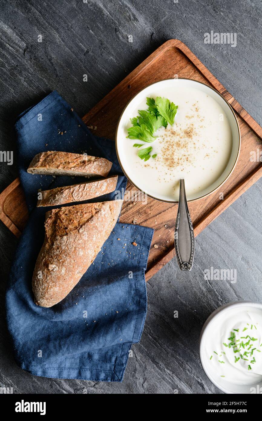 Delicious creamy celery soup topped with black pepper and fresh leaves, served with crusty bread, on rustic stone background Stock Photo