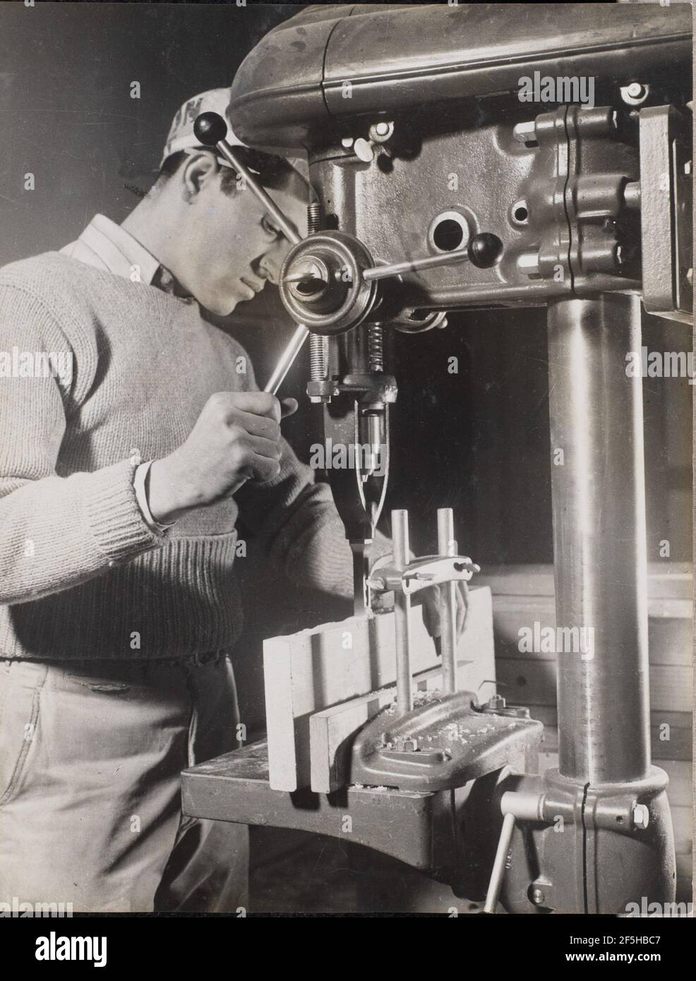 Man uses a machine to drill holes in two wood blocks. Arnold Eagle