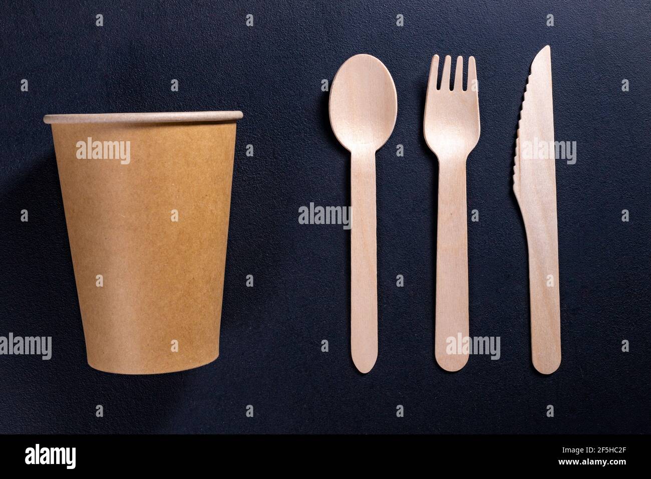 Disposable wooden cutlery and cardboard containers. Accessories for eating outdoors. Dark background. Stock Photo