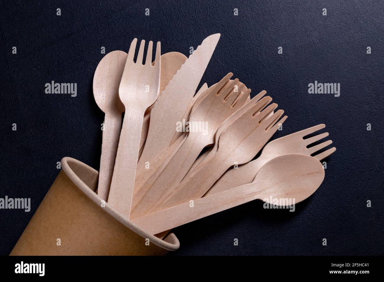 Disposable wooden cutlery and cardboard containers. Accessories for eating outdoors. Dark background. Stock Photo