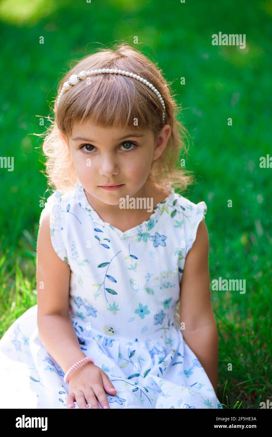 Portrait of a smiling little girl sitting on green grass Stock Photo ...
