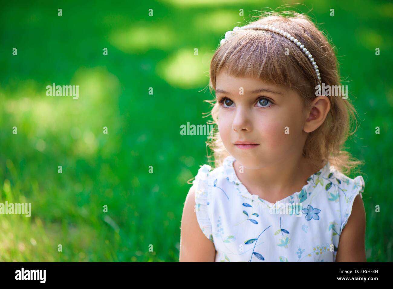 Portrait of a smiling little girl sitting on green grass Stock Photo ...