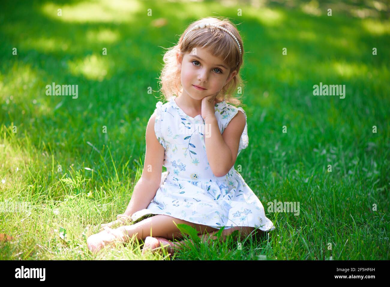 Portrait of a smiling little girl sitting on green grass Stock Photo ...