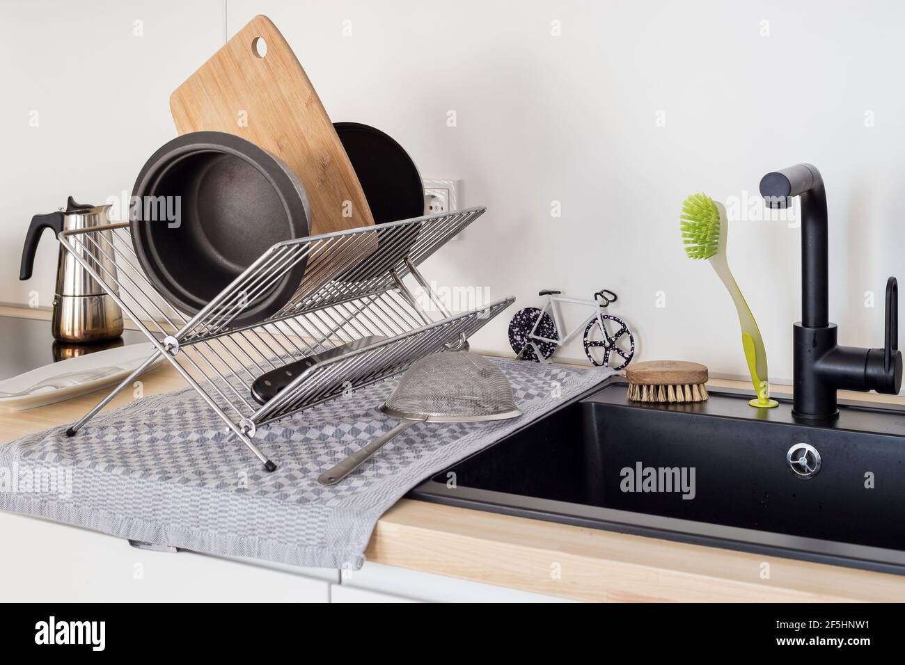 Modern kitchen sink with drying rack holding cookware, chopping board and utensils after washing, clean domestic interior. Stock Photo