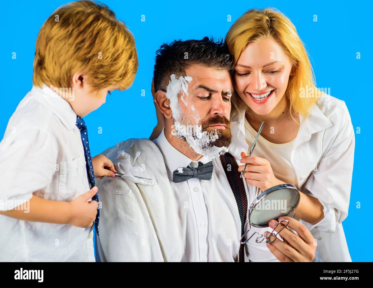 Hairdresser making hairstyle. Family day. Mother cutting hair to father and little son shaving dad beard with razor. Stock Photo