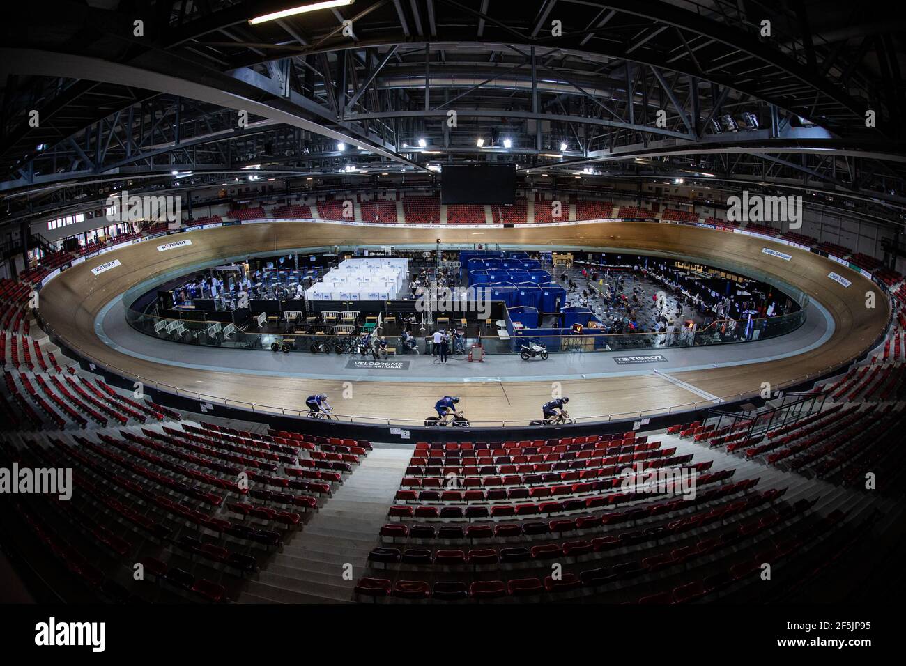 Paris, Paris in France. 26th Mar, 2021. France's national cycling team train as people wait to receive COVID-19 vaccine at the national velodrome used as a COVID-19 vaccination centre in Saint-Quentin-en-Yvelines, southwest of Paris in France, on March 26, 2021. As of Friday, 7,519,740 people in France -- or 14.3 percent of the adult population -- had received at least one COVID-19 vaccine dose, and 2,653,261 people -- 5.1 percent of the adult population -- both doses, the Health Ministry said. Credit: Aurelien Morissard/Xinhua/Alamy Live News Stock Photo
