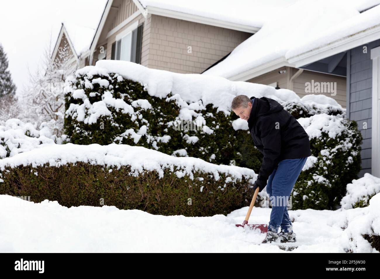 Mature man shoveling snow off sidewalk in front of home Stock Photo