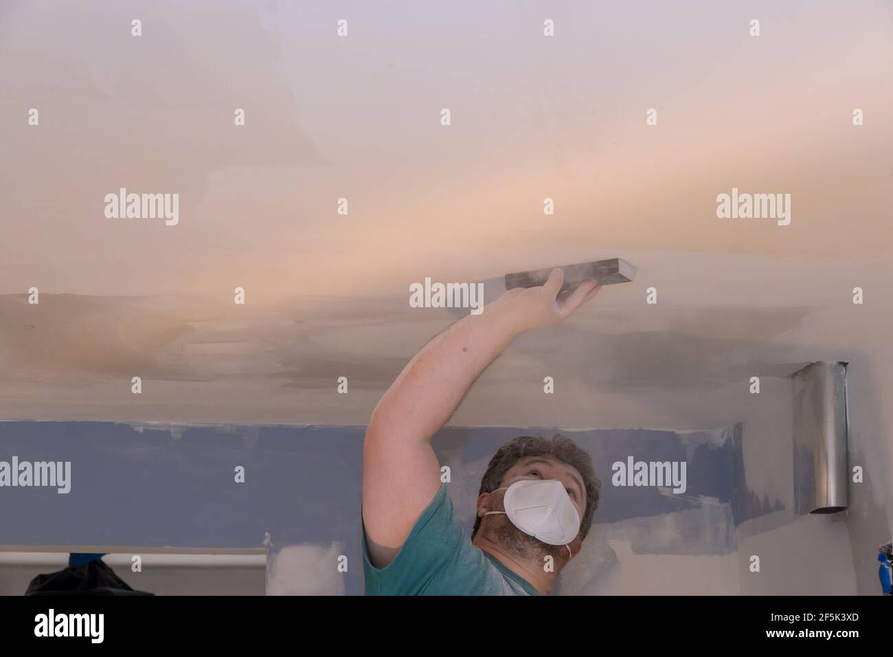 Contractor using sand trowel sanding the the plaster plasterboard drywall ceiling during room