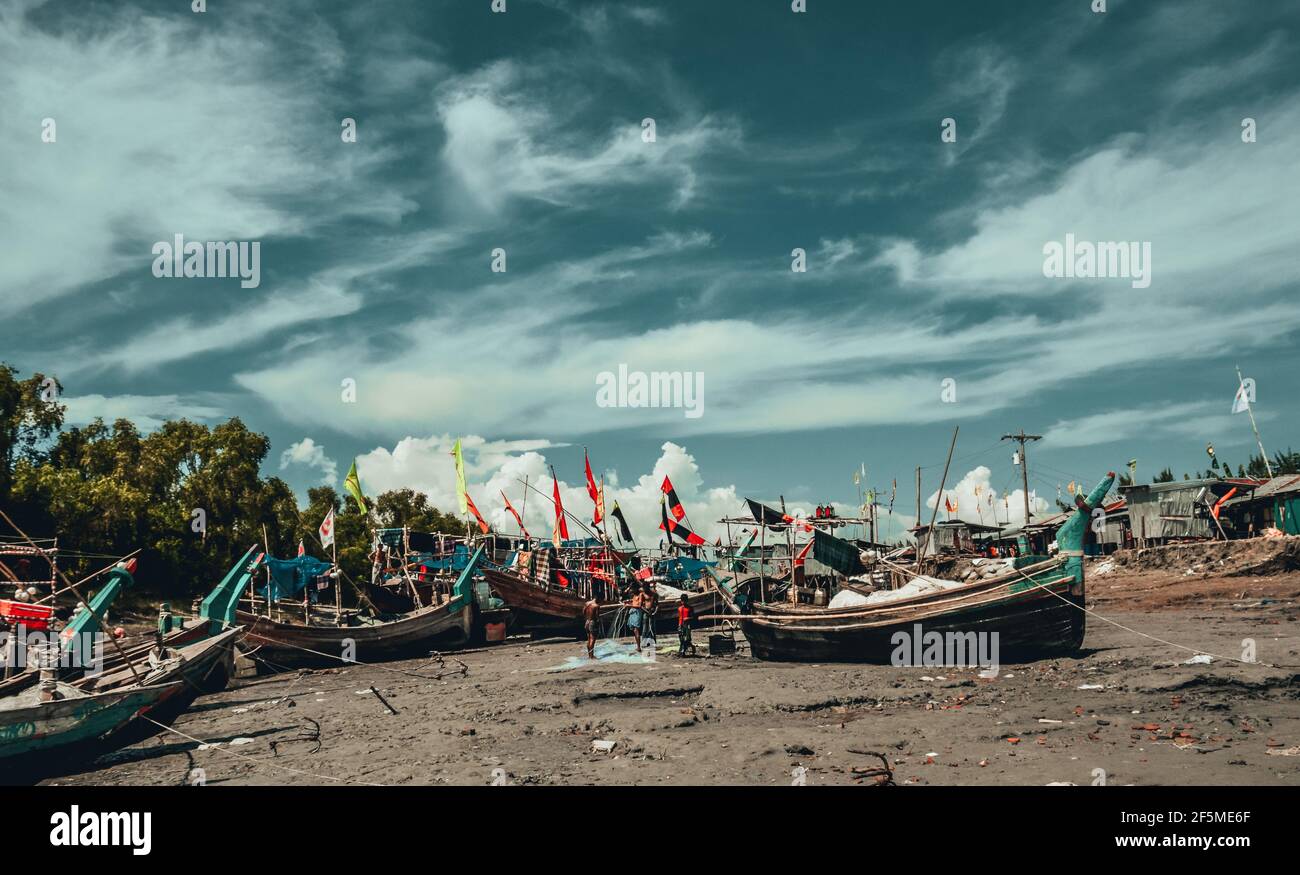 Riverside fishing boats and fisherman and color graded sky with clouds Stock Photo
