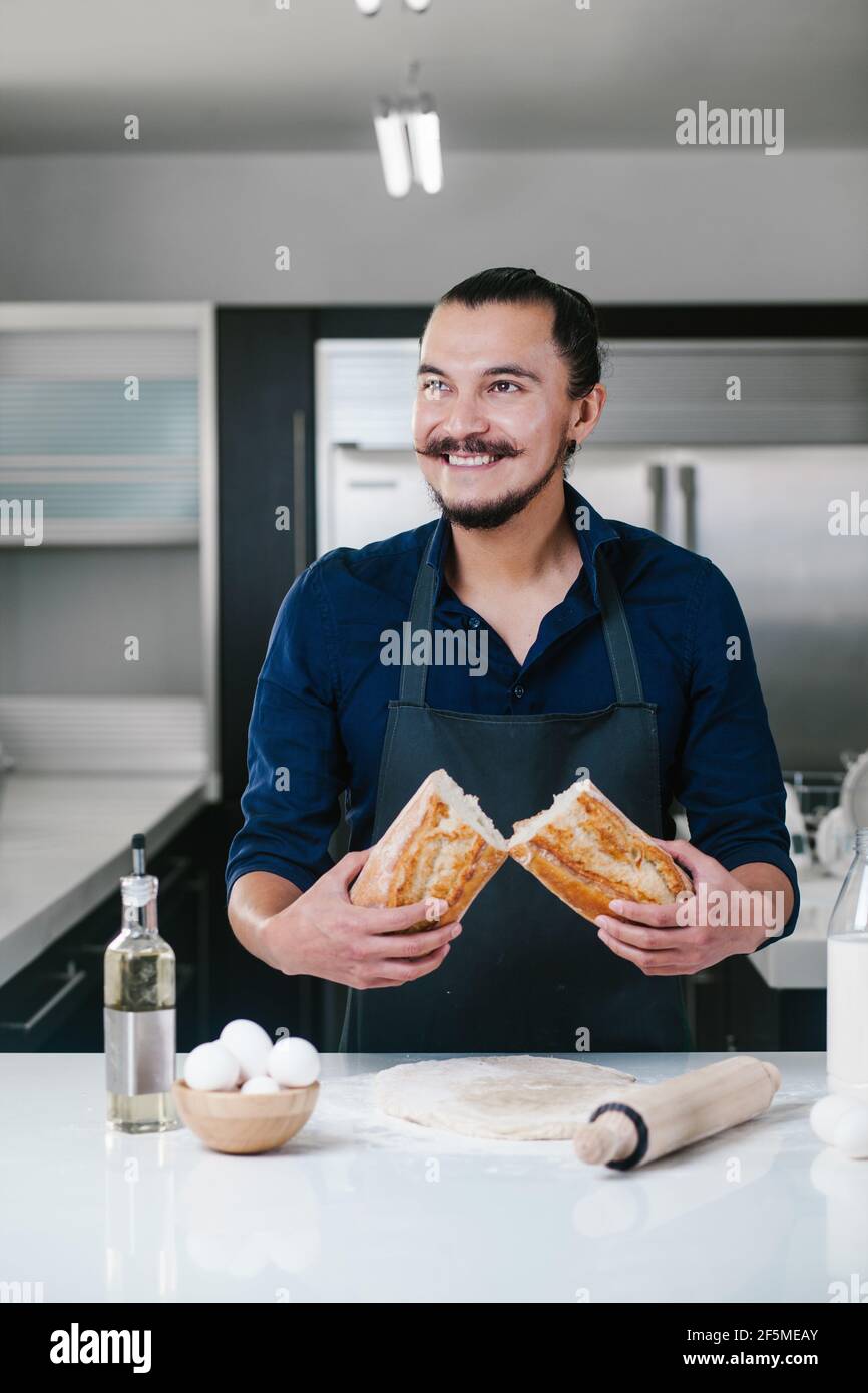 portrait of Latin man baking and holding bread at kitchen in Mexico city Stock Photo