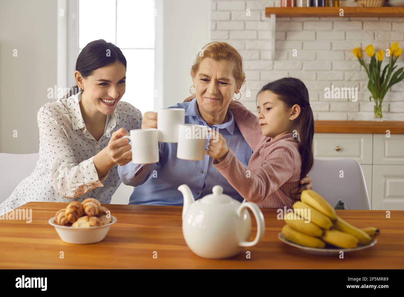 Three generations of women of one family drinking tea together sitting at home in the kitchen. Stock Photo