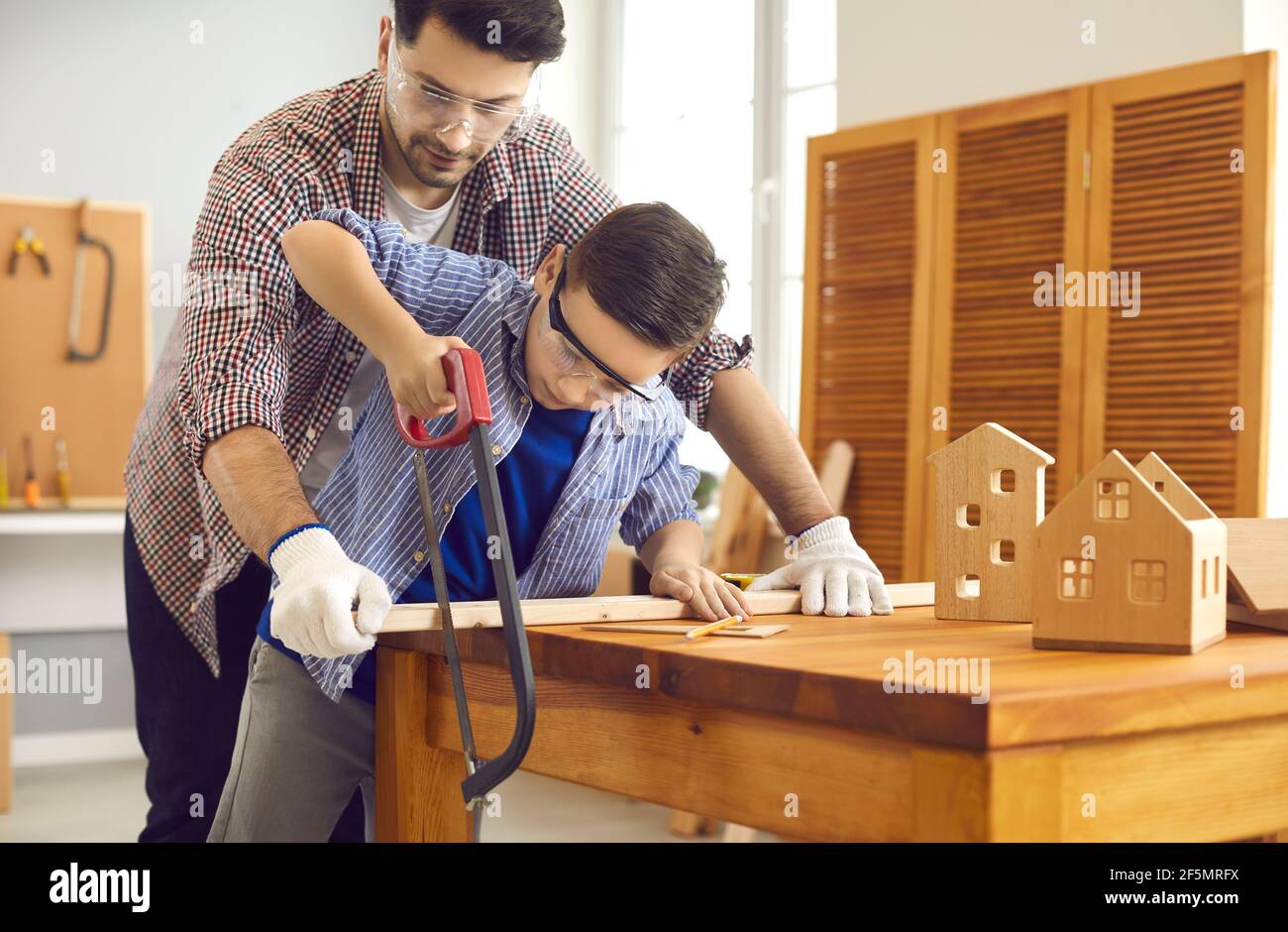Father teaching son use sharp handsaw for woodworking at home carpentry workshop Stock Photo