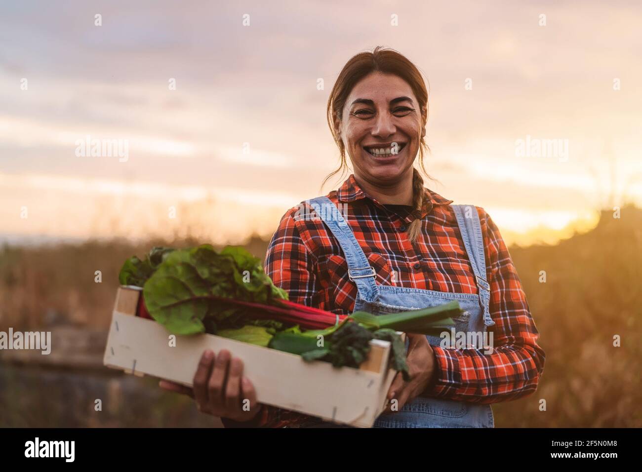 Happy female farmer holding a wood box containing fresh vegetables ...